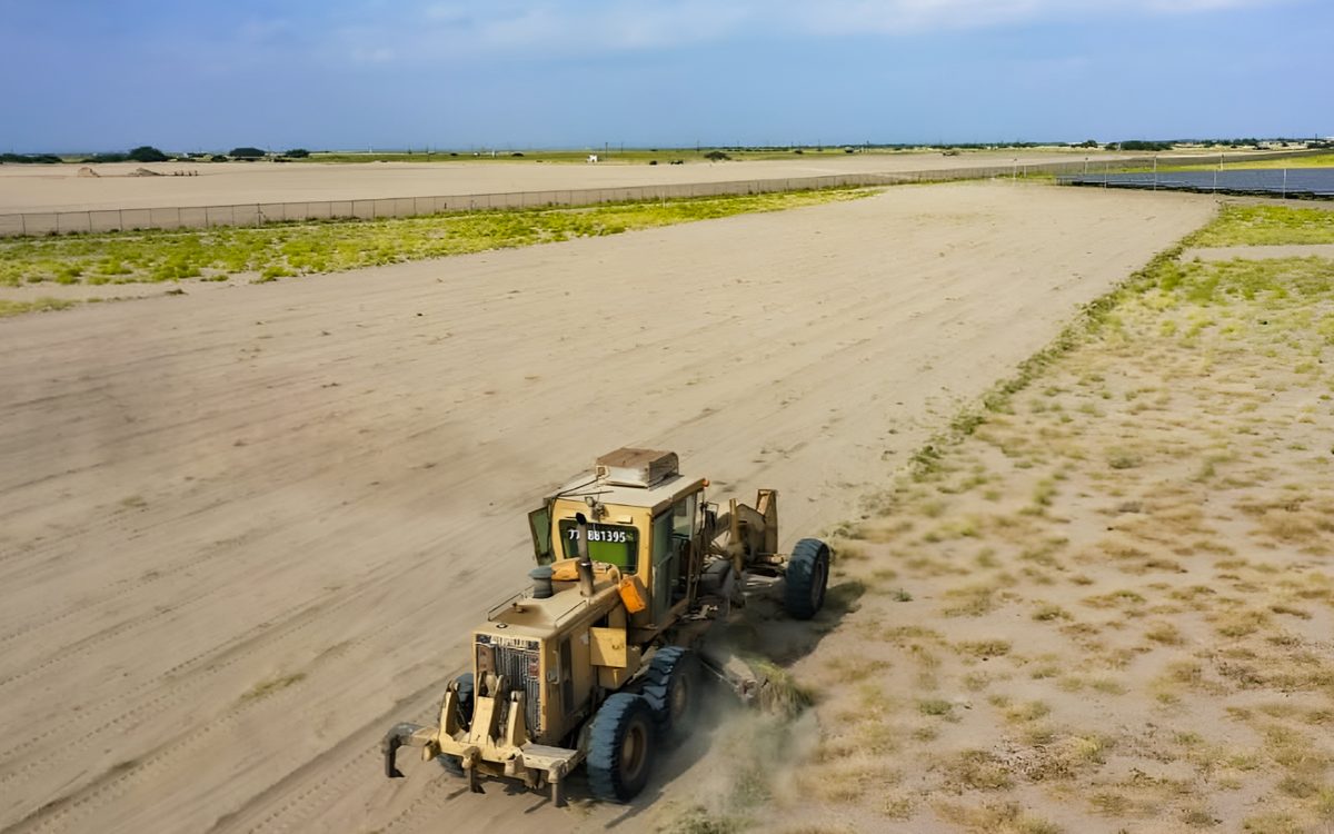 A grader working the cleared Aden Phase II site beside the existing solar park