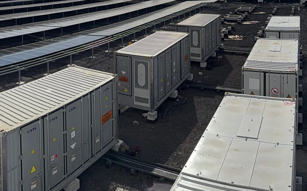 Rows of battery energy storage containers on a prepared pad beside a solar plant