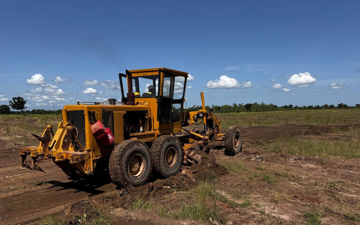 A motor grader preparing the Dialakoro site under a broken sky, Mali