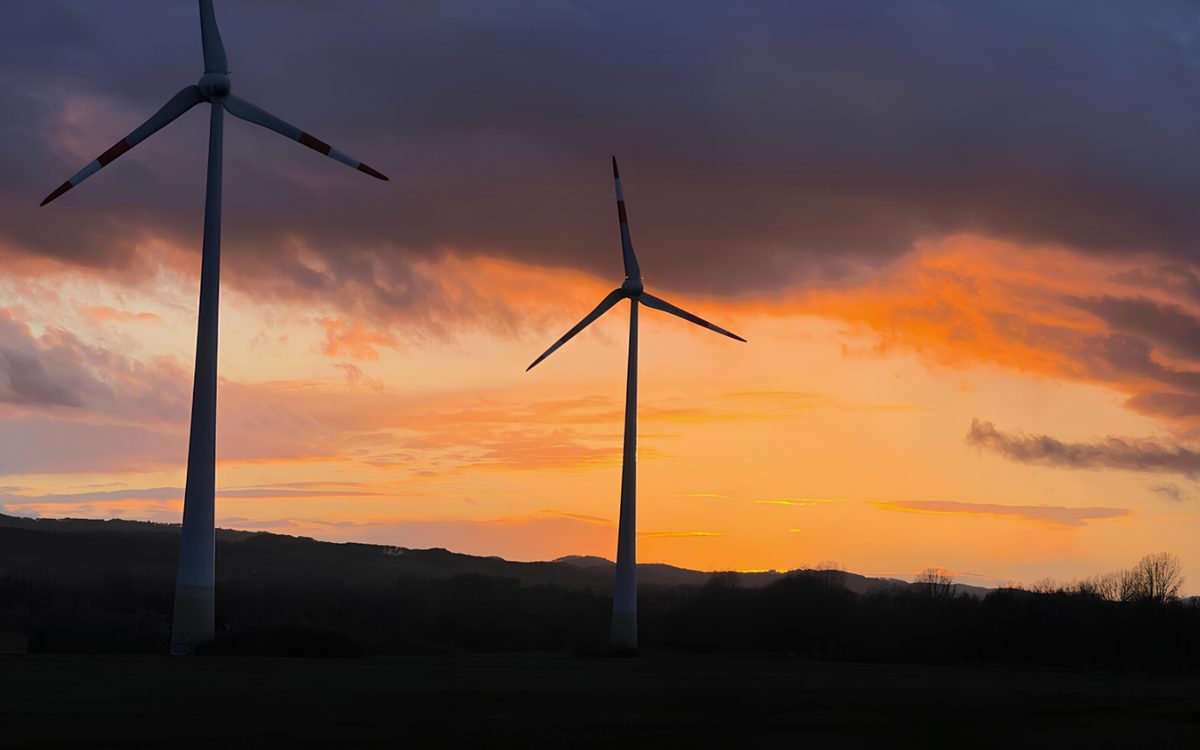 A wind turbine silhouetted against an orange sunset sky
