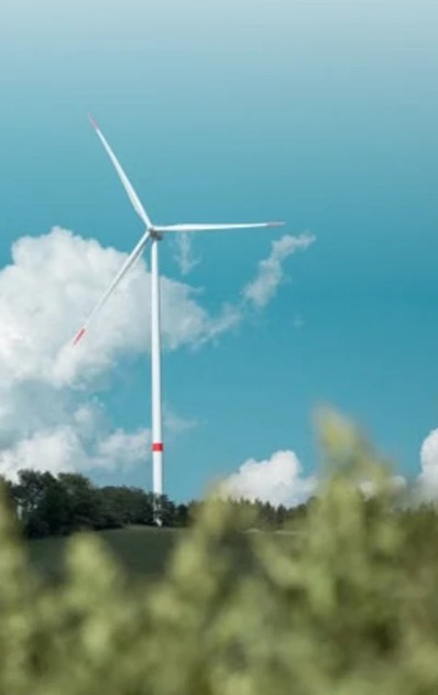 A wind turbine against a teal sky above green foliage